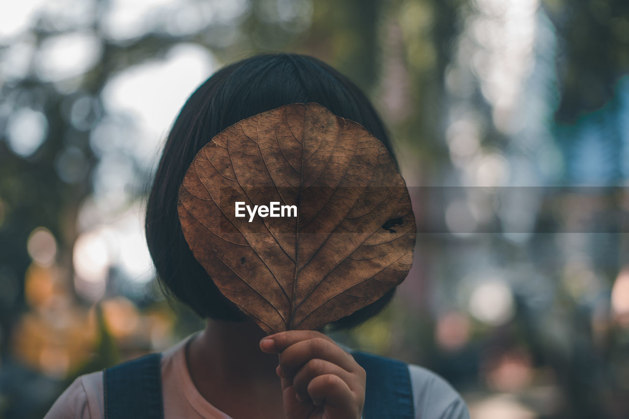 Close-up of woman hiding face with autumn leaf 