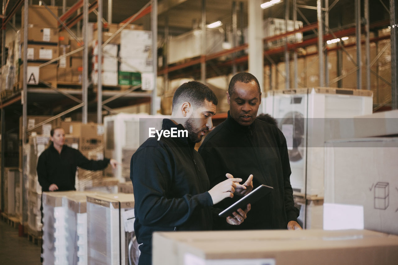 Male manual workers discussing over digital tablet at warehouse