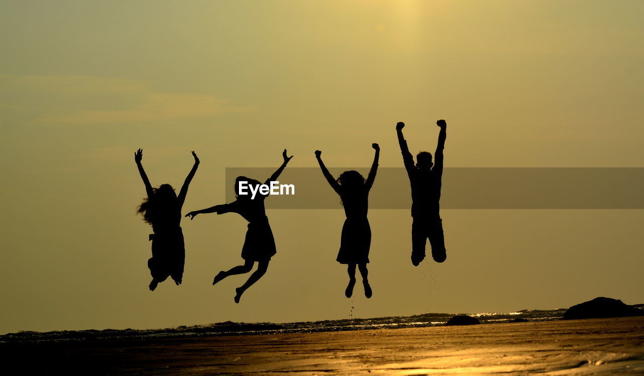 Silhouette friends jumping at beach against sky during sunset