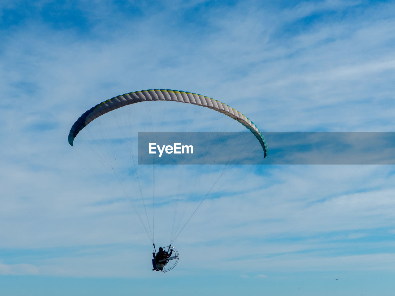 Low angle view of man paragliding against cloudy sky
