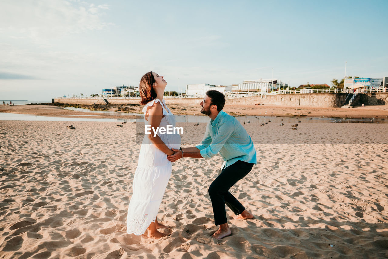 Couple holding hands standing on beach against sky