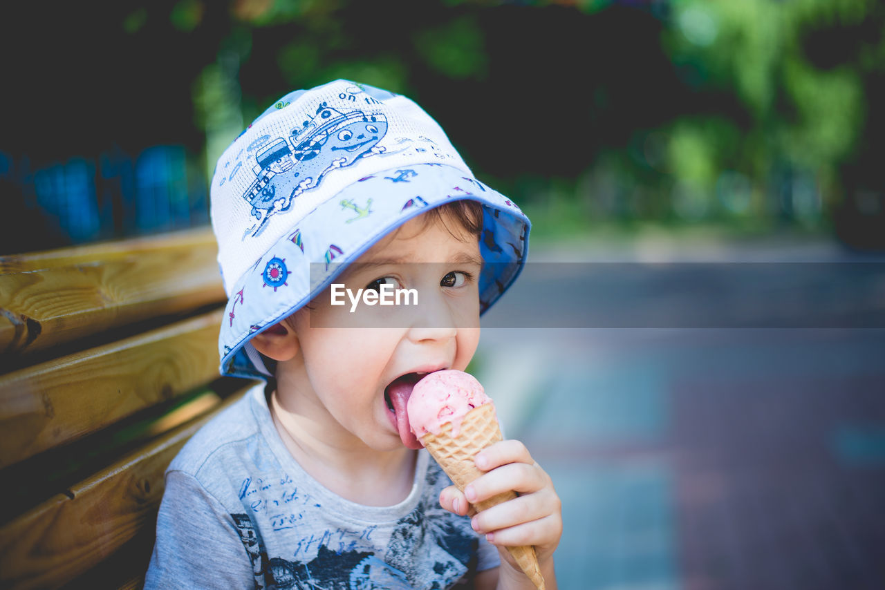Portrait of cheerful boy eating ice cream while sitting on park bench