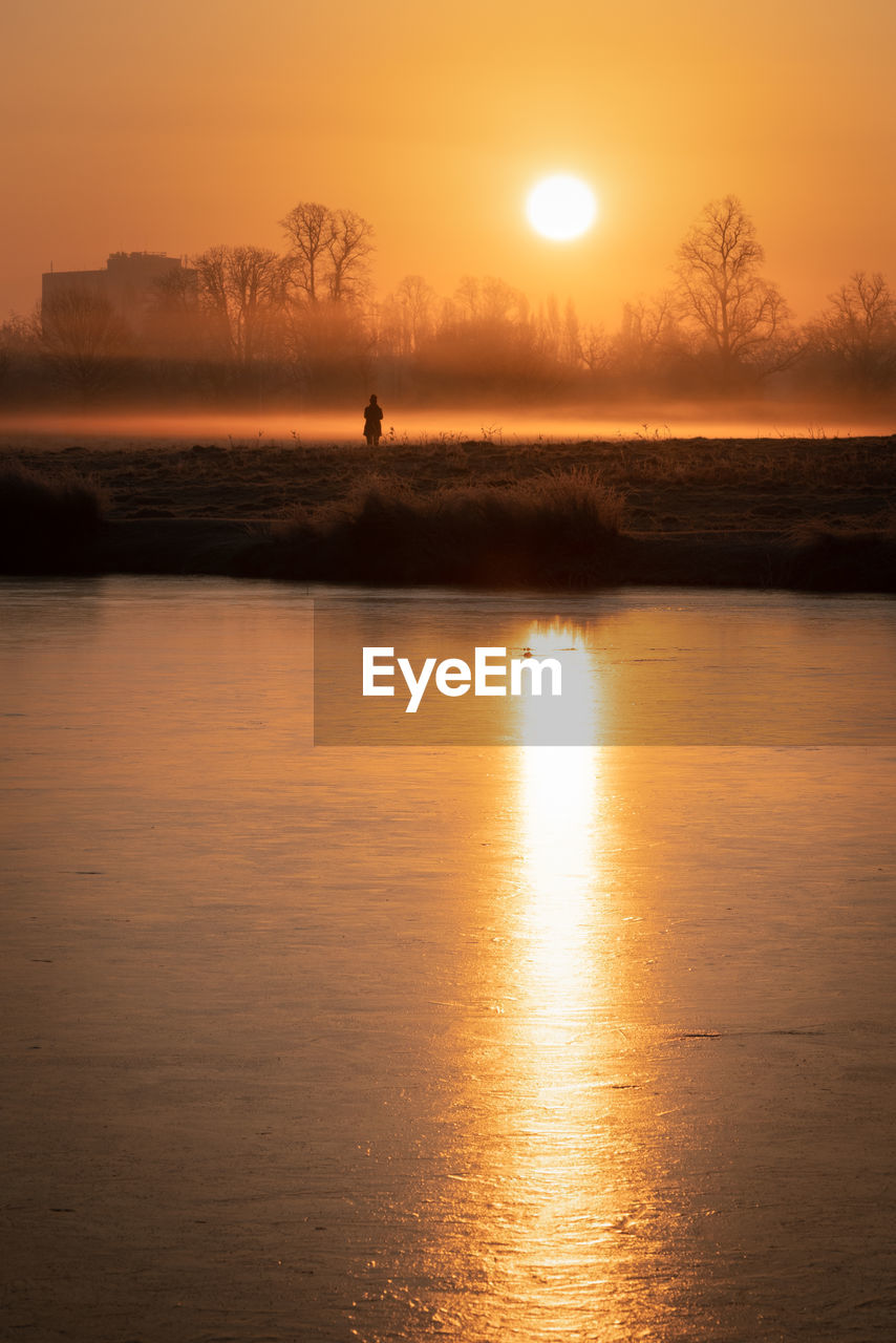 Golden sunrise reflected in lake in bushy park, london, with one person standing, watching in awe