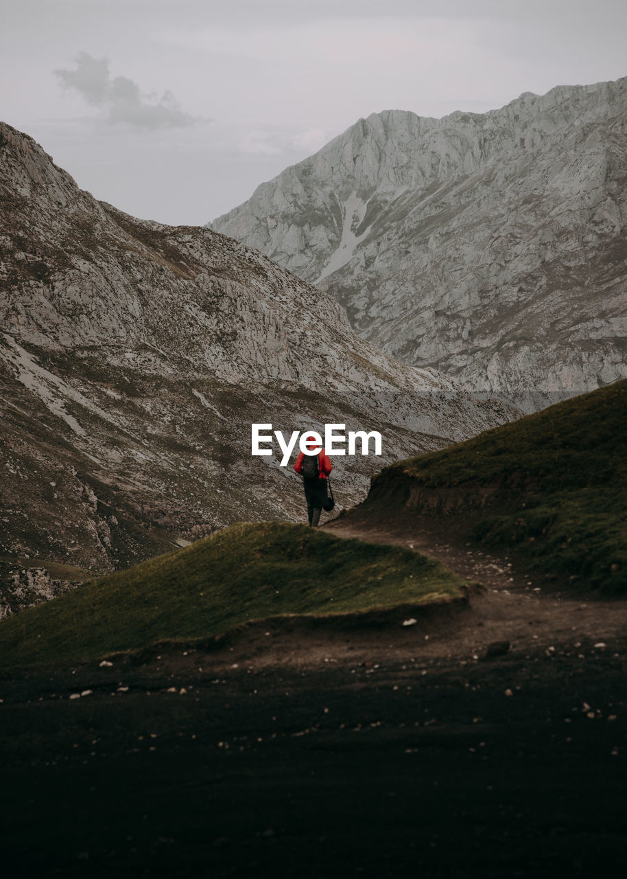 Rear view of hiker walking on mountain against sky