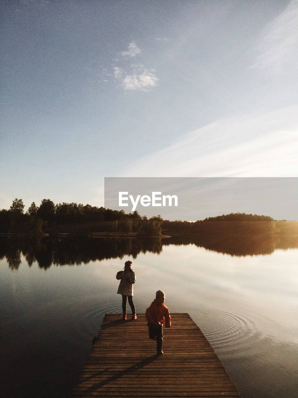 Playful sibling on pier against lake during sunset