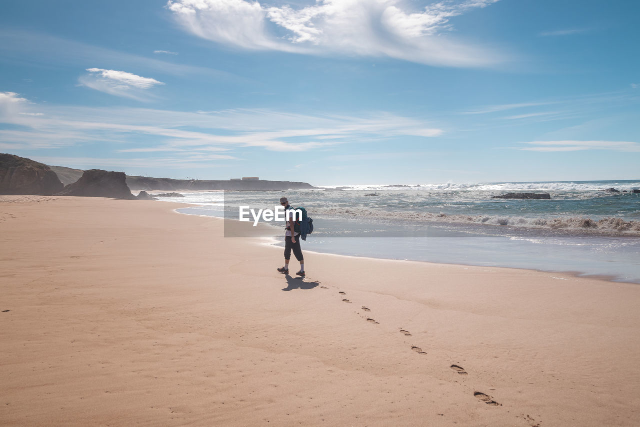 rear view of woman walking on beach against sky