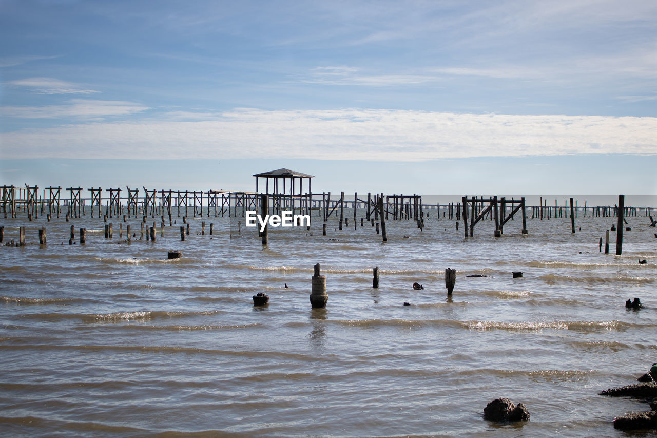 Wooden posts in sea against sky