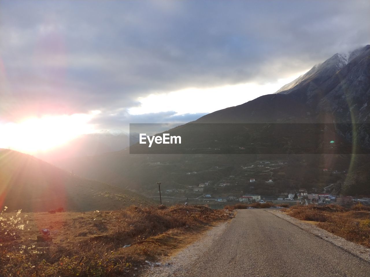 ROAD LEADING TOWARDS MOUNTAINS AGAINST BRIGHT SUN