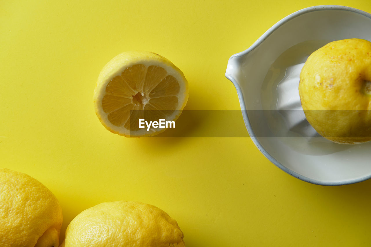 Squeezing a lemon in a white ceramic juicer on a yellow background