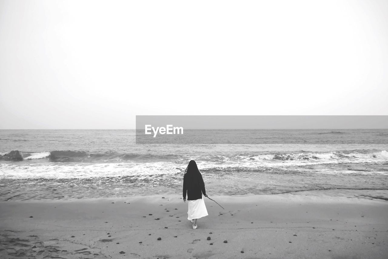 Rear view of woman walking at beach against clear sky