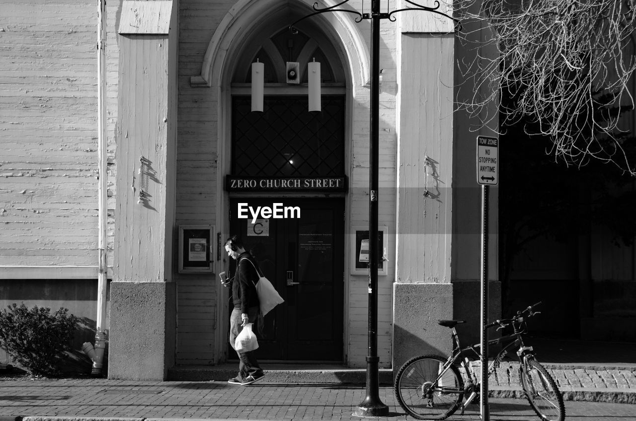 Side view of man walking against building on sunny day