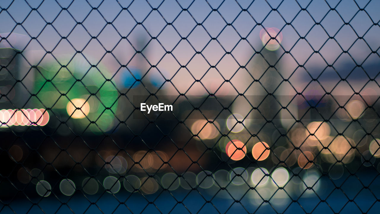 Close-up of chainlink fence against sky during sunset