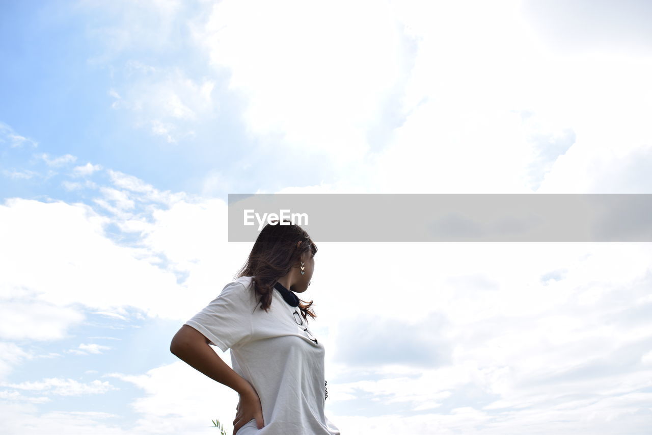 Low angle view of woman standing with hand on hip against cloudy sky