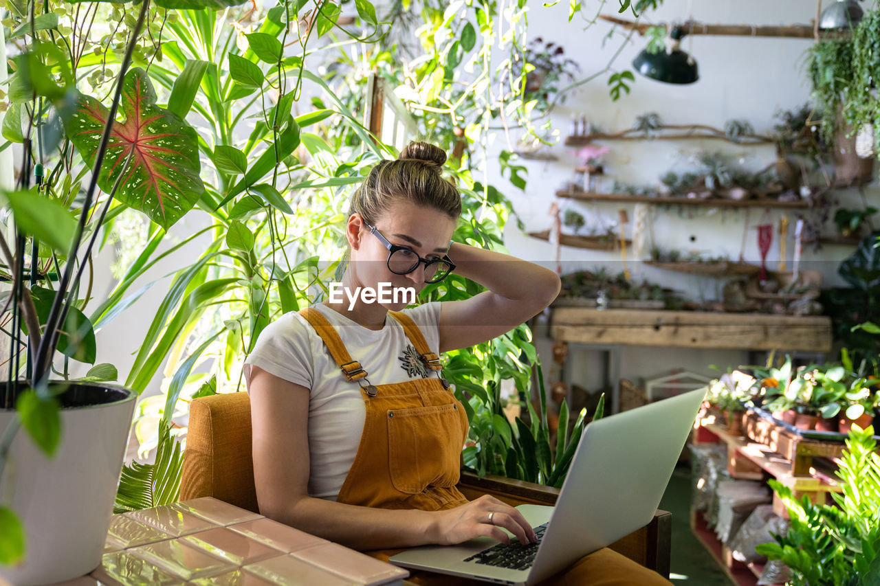 Woman using laptop while sitting amidst plants in workshop