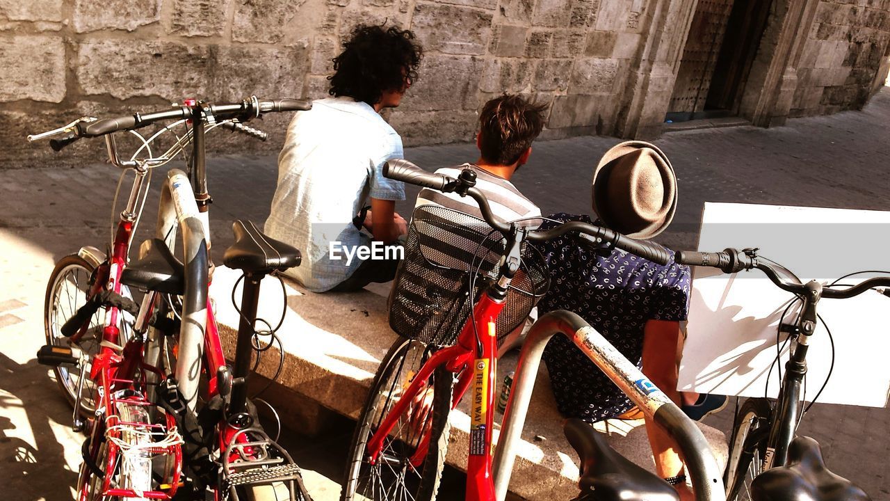 Rear view of friends sitting by bicycles parked on footpath