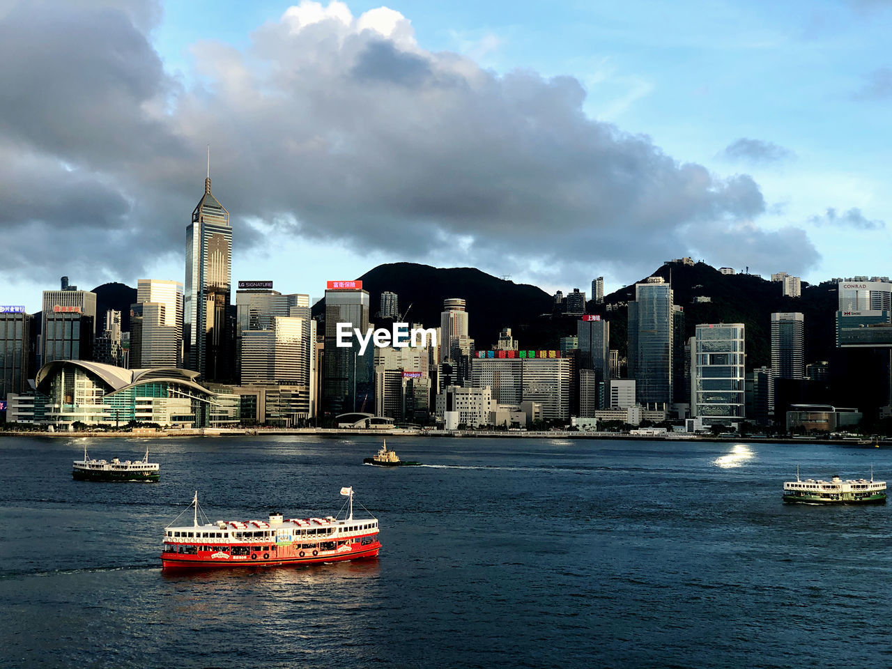 Ferry in victoria harbour by buildings against sky in hong kong