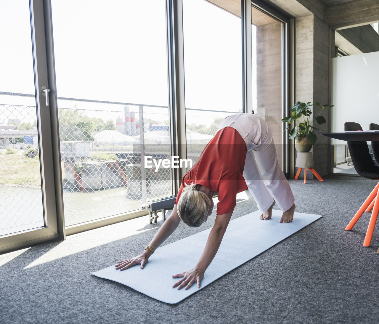 Businesswoman practicing adho mukha svanasana on exercise mat in office