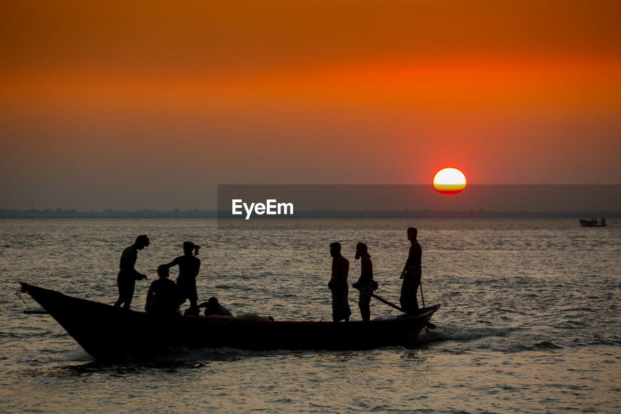 Silhouette people in river against sky during sunset