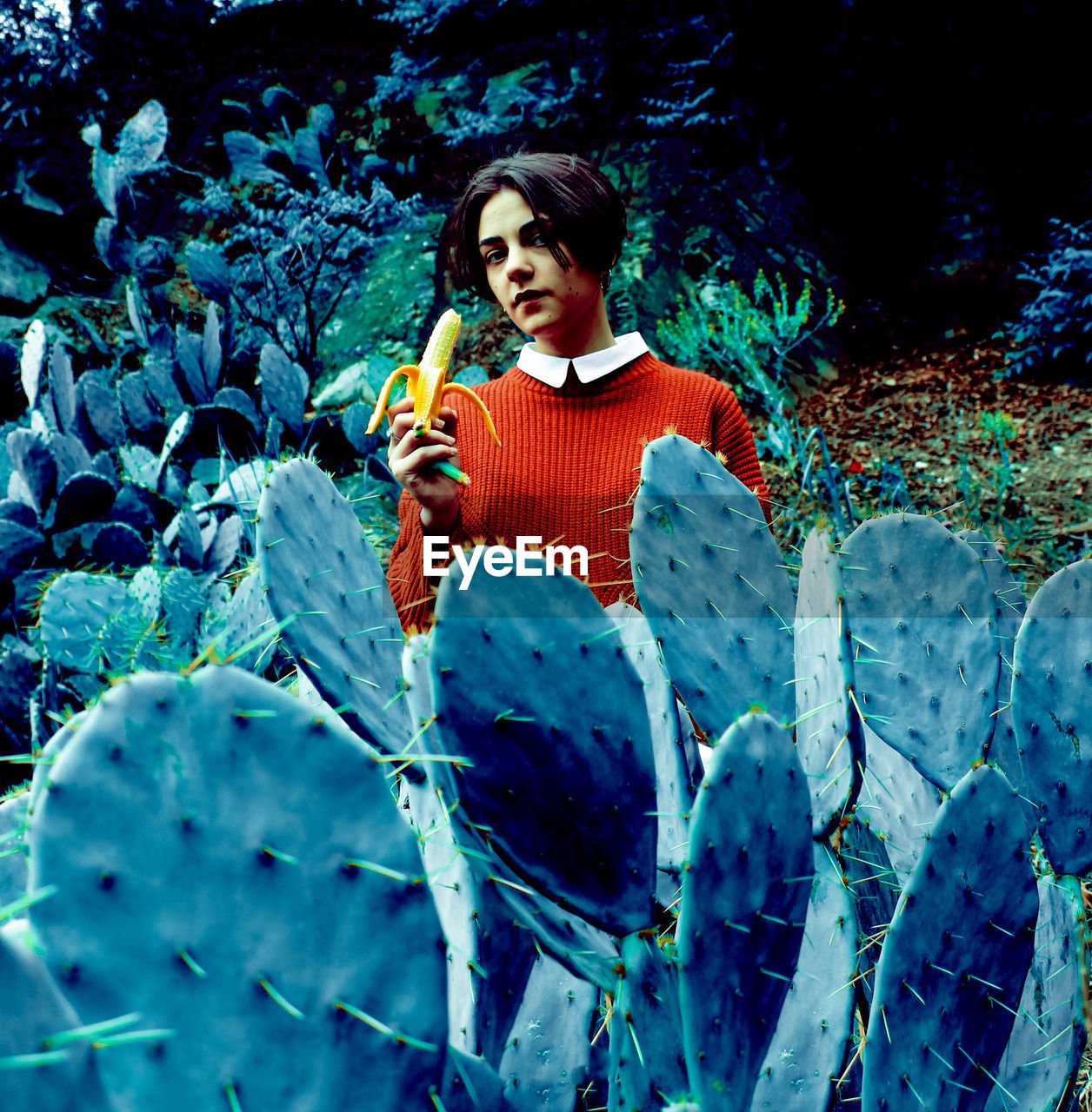 Portrait of woman eating banana while standing against cactus plants
