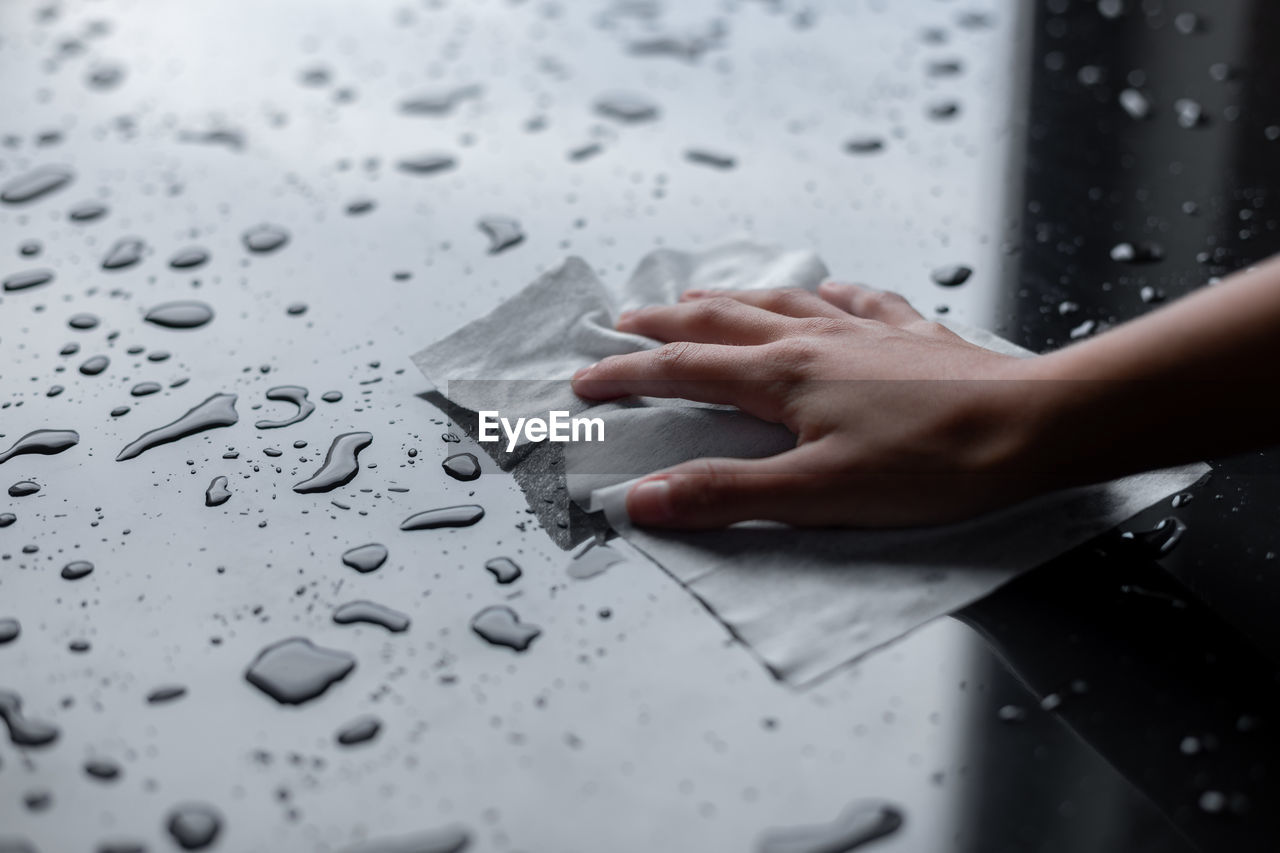 CLOSE-UP OF HUMAN HAND TOUCHING WET PAPER ON TABLE