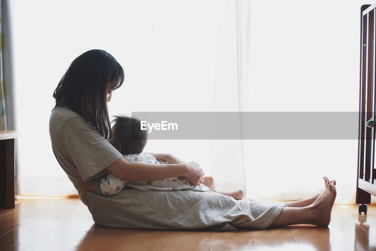Side view of mother and baby sitting on floor at home