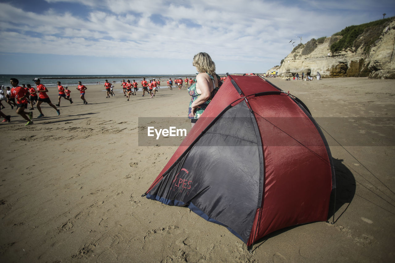 Rear view of woman standing by tent on beach against sky