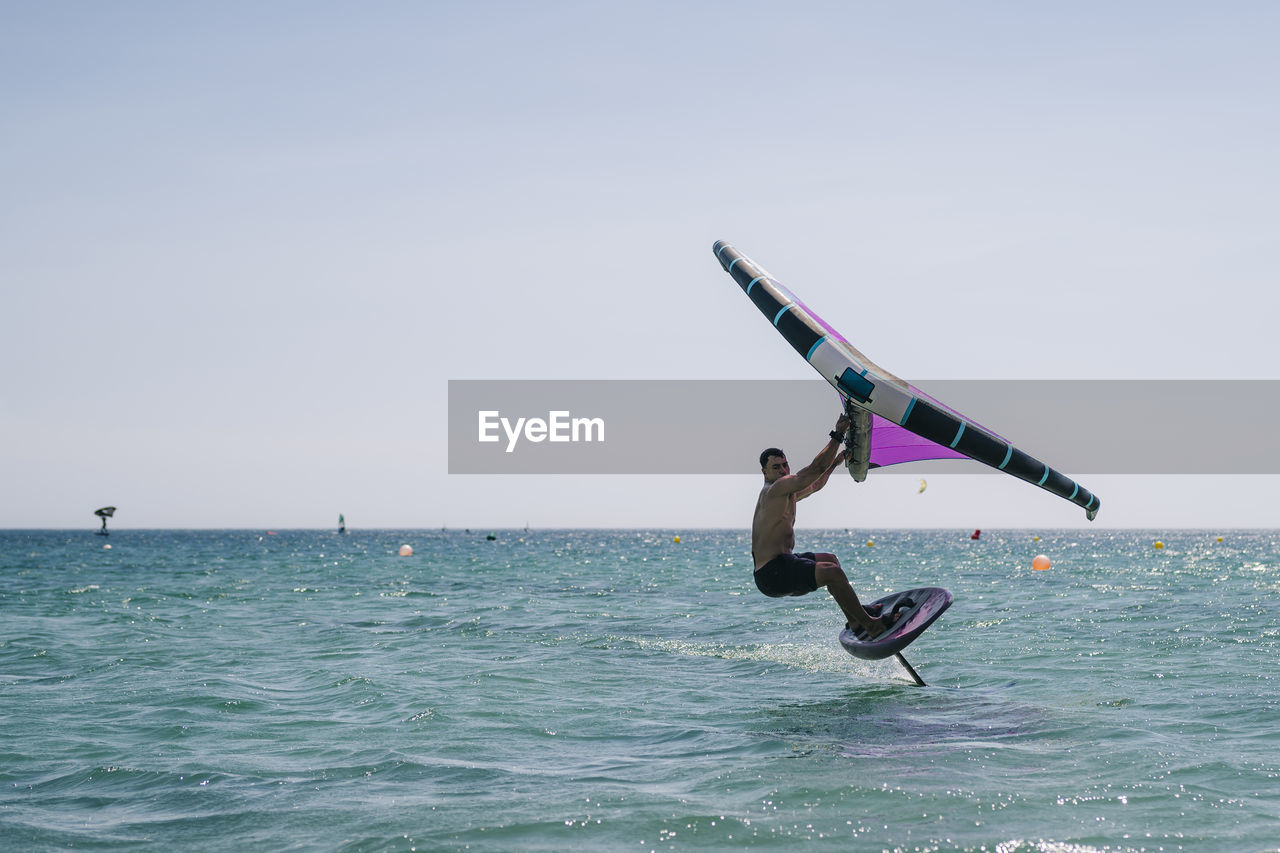 Young shirtless man practicing wind foil in sea