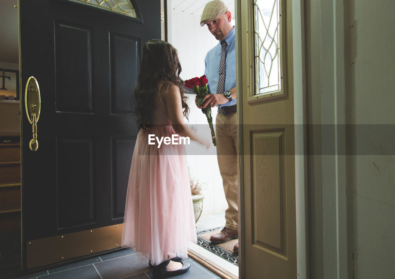 Father giving roses to daughter wearing pink dress at doorway