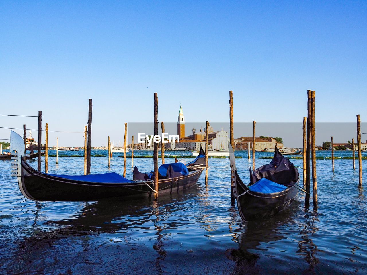 Gondolas moored in canal against sky
