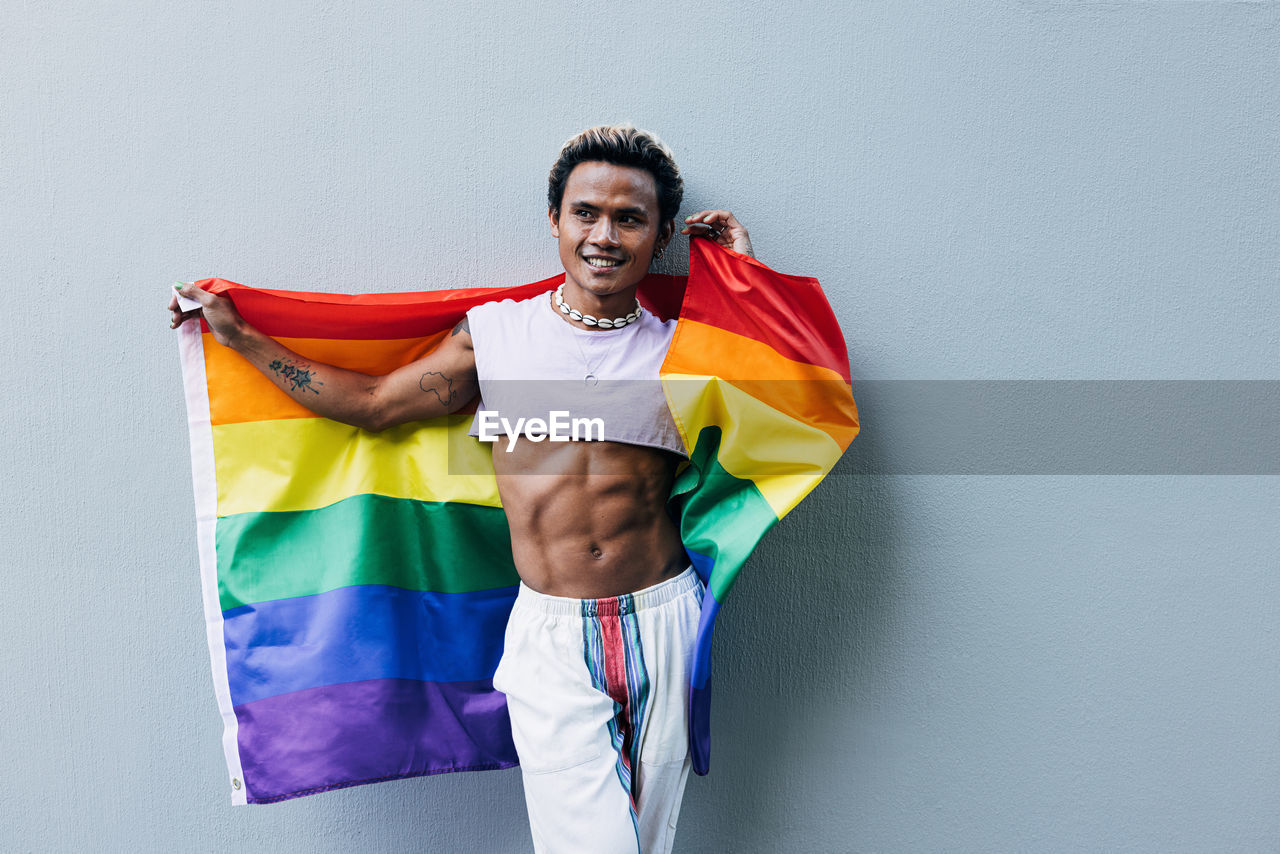 Man with rainbow flag standing against wall