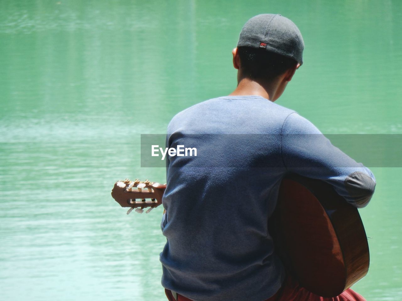 Rear view of man sitting with guitar against sea