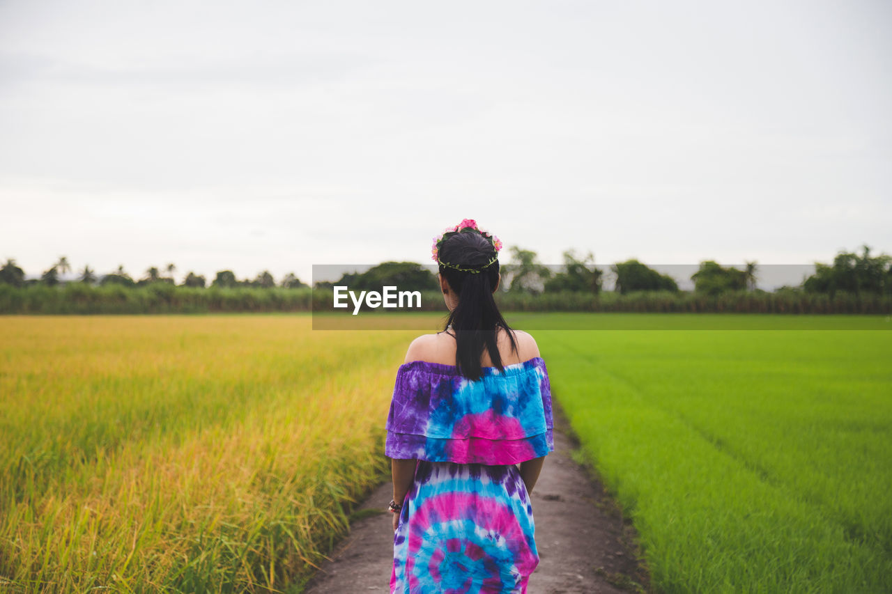 Rear view of woman standing on field against sky