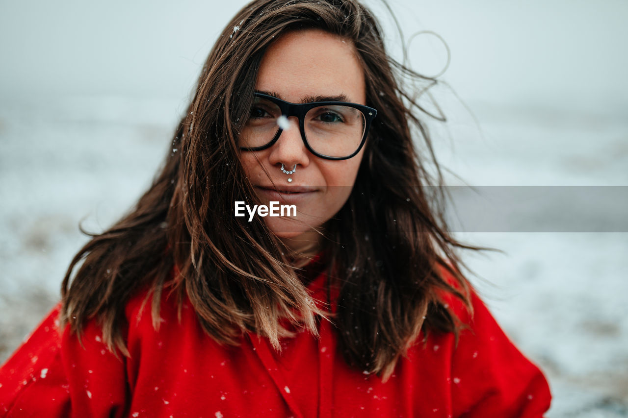 Young happy tourist in eyeglasses with piercing looking at camera between deserted ground in snow
