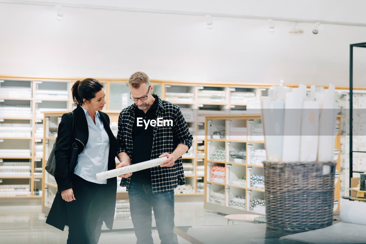 Salesman showing wallpaper to female customer in store