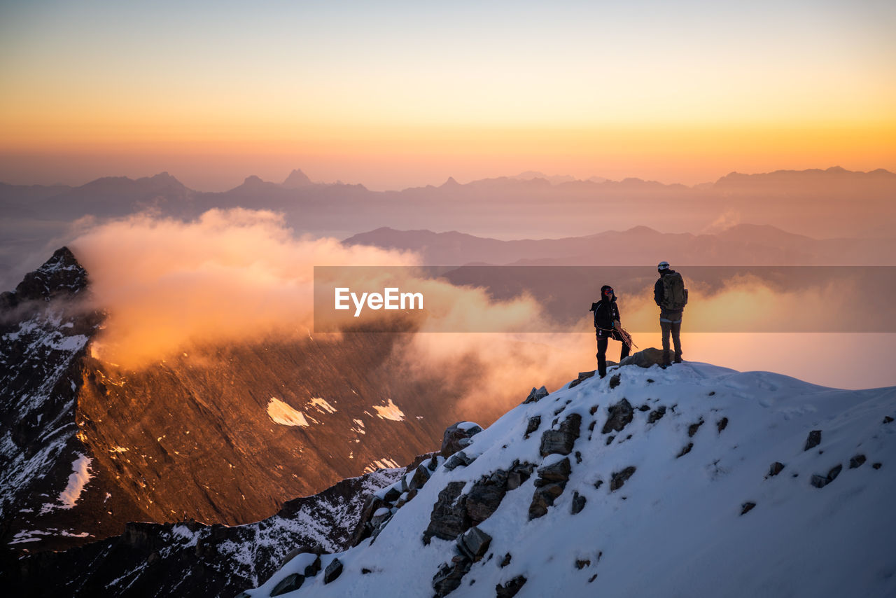 People standing on snowcapped mountain against sky during sunrise