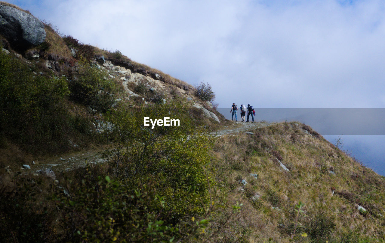 PEOPLE WALKING ON MOUNTAIN ROAD AGAINST SKY