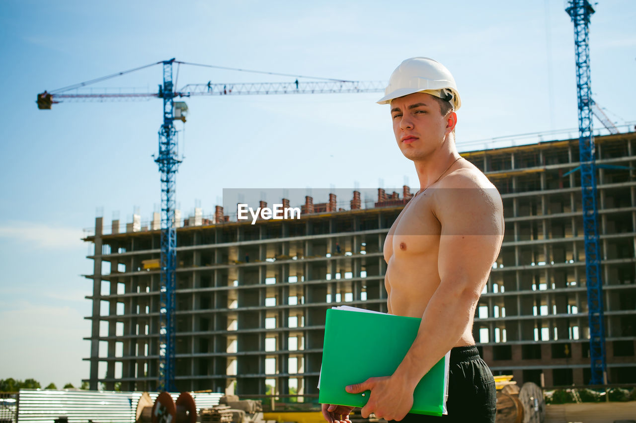 Shirtless man standing against construction buildings