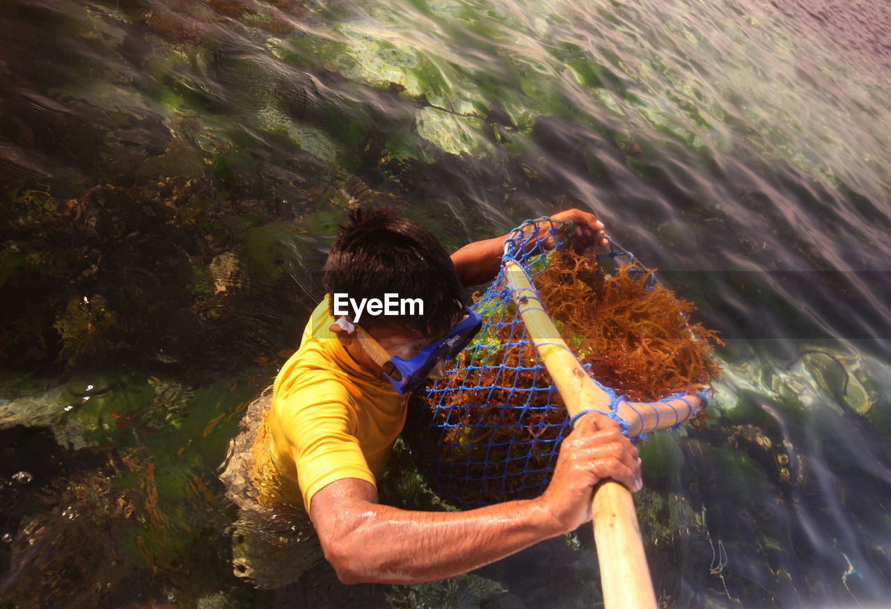 Man holding fishing net with coral in sea