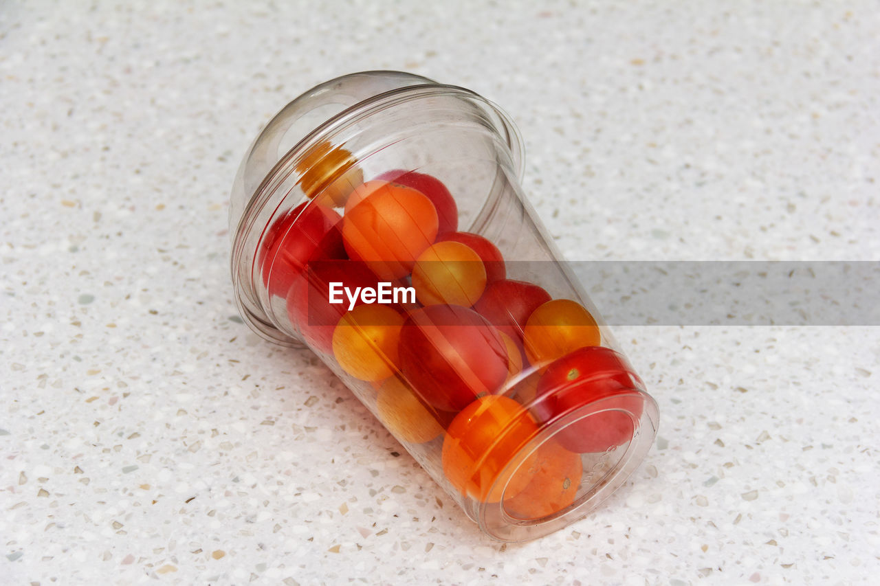 Small red and yellow tomatoes in a plastic transparent glass are lying on the table close-up