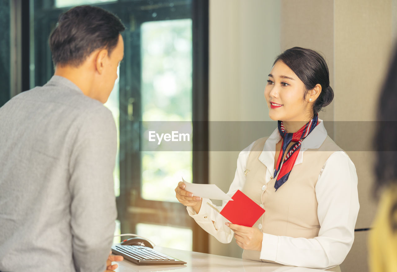 At the airport check-in counter, a passenger hands over his documents to the manager via a counter 