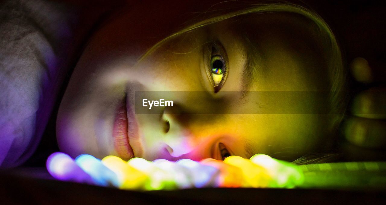Close-up portrait of young woman lying by colorful illuminated lighting equipment