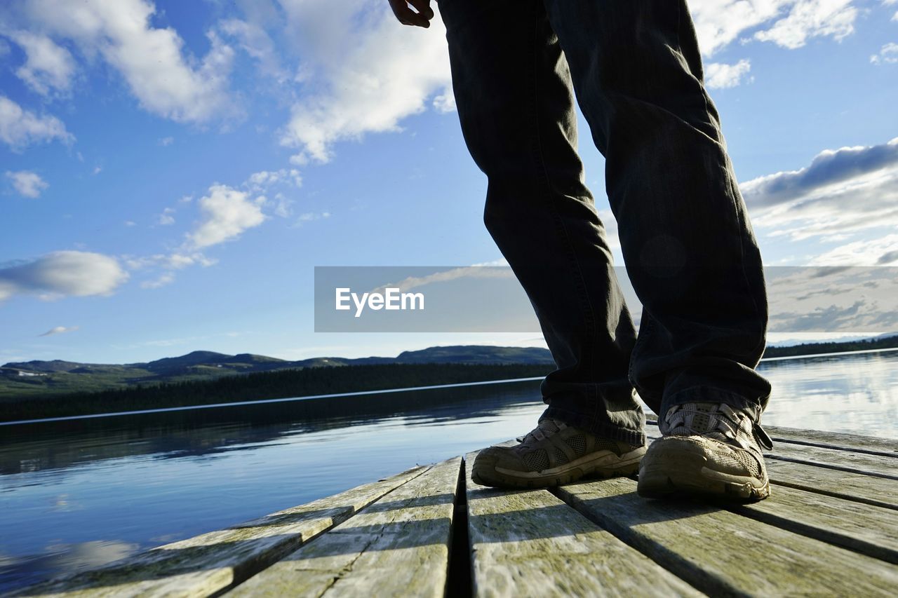 Low section of man standing by lake against sky