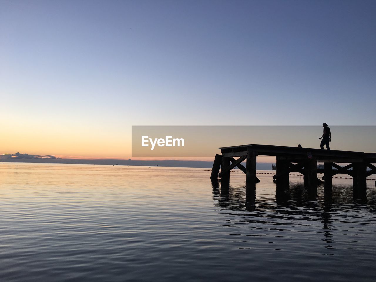 Silhouette person standing on pier over sea against clear sky during sunset