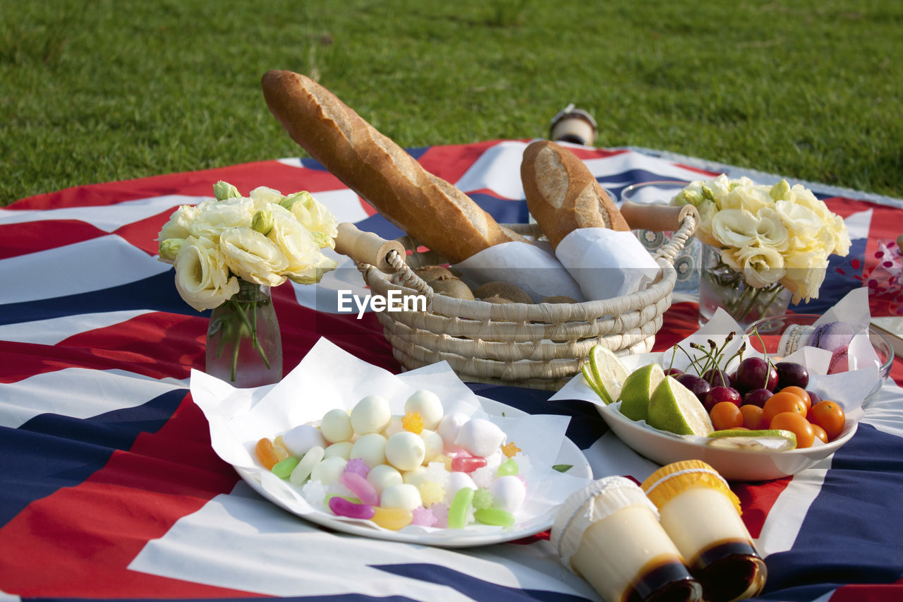 Clise-up of breads, candies, flowers, puddings on the picnic blanket on the grass.