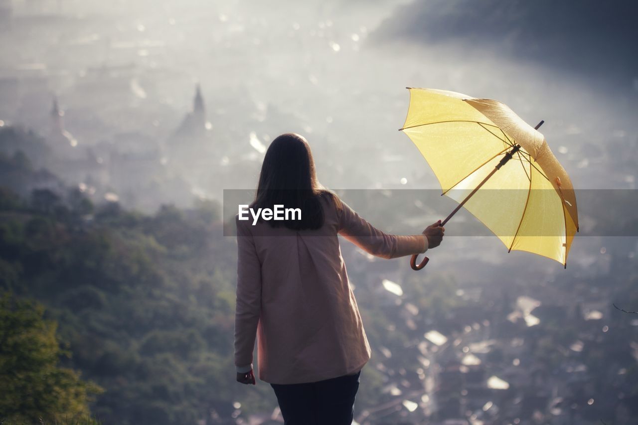 Rear view of woman holding umbrella against mountain