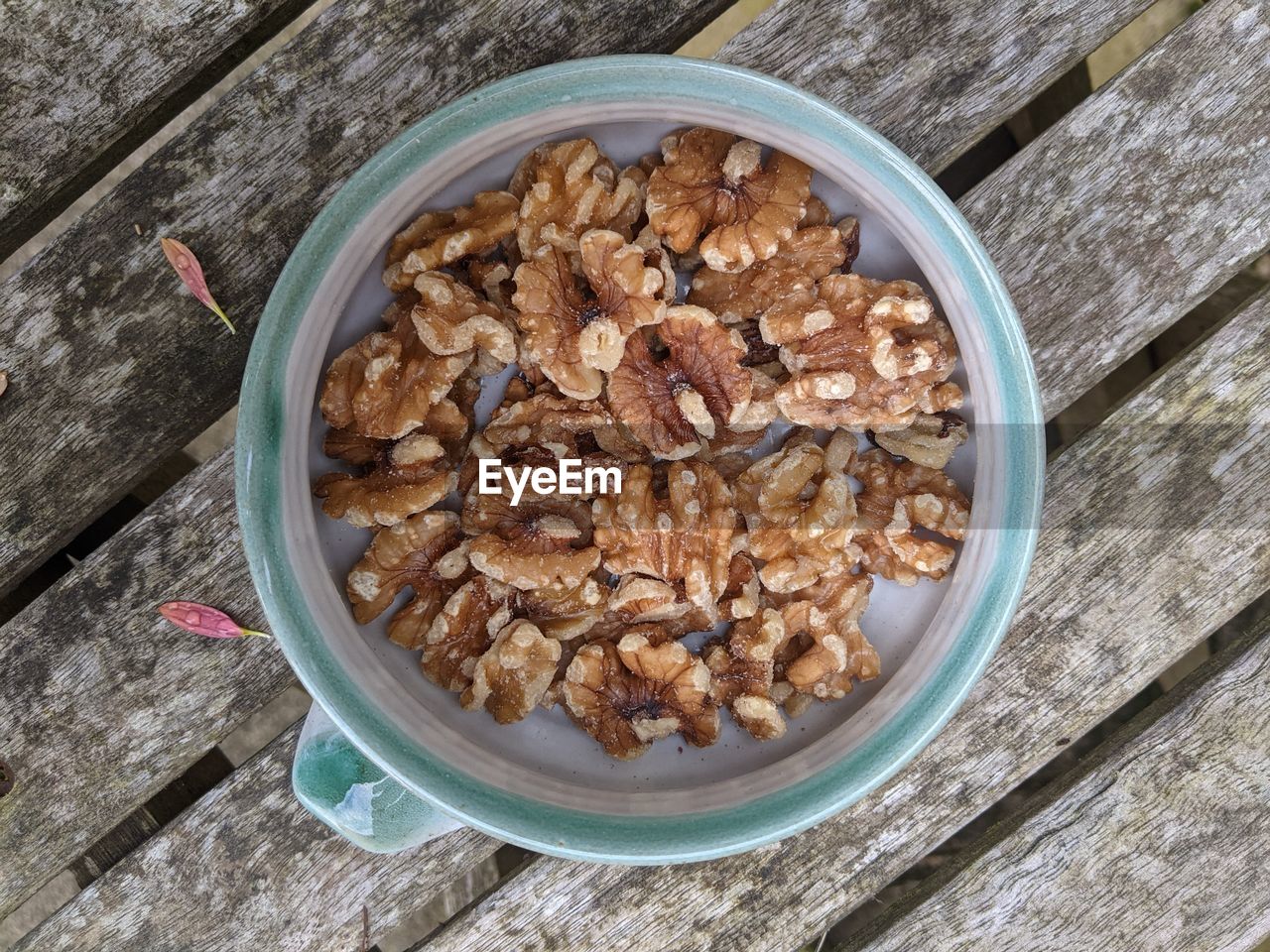 A bowl of walnuts viewed from above, lying on a wooden bench.