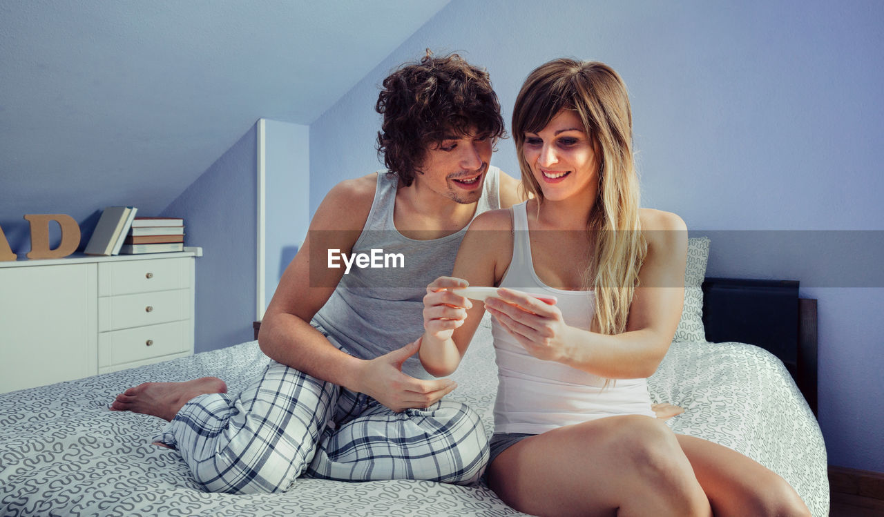 Cheerful couple with pregnancy test on bed at home