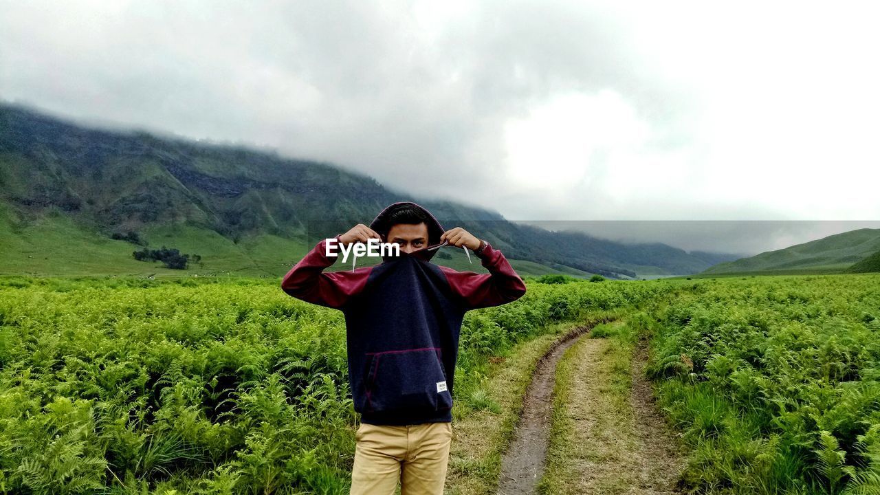 Portrait of young man standing amidst plants on field during foggy weather