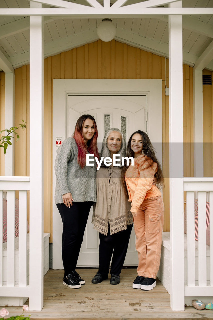 Portrait of smiling senior woman with daughter and granddaughter standing at porch