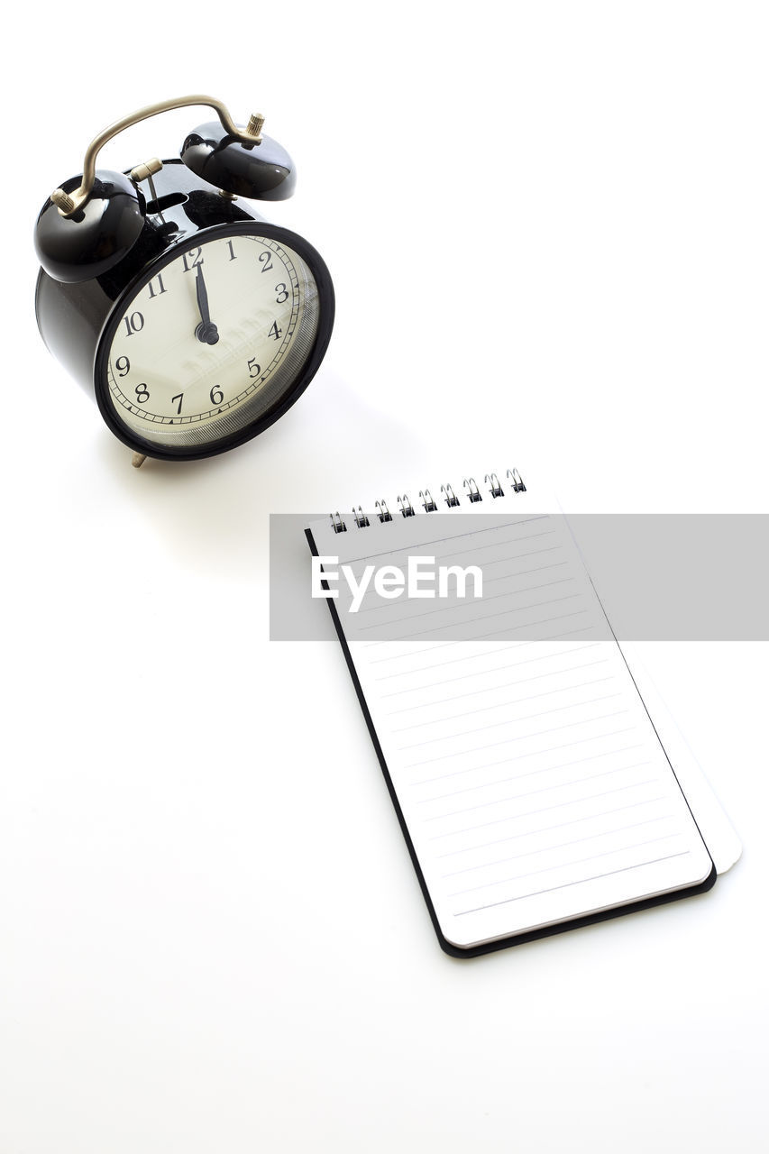 High angle view of alarm clock and note pad against white background